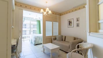 Una habitación con sofá, una mesita, una silla de mimbre, ventana con persianas y un candelabro.