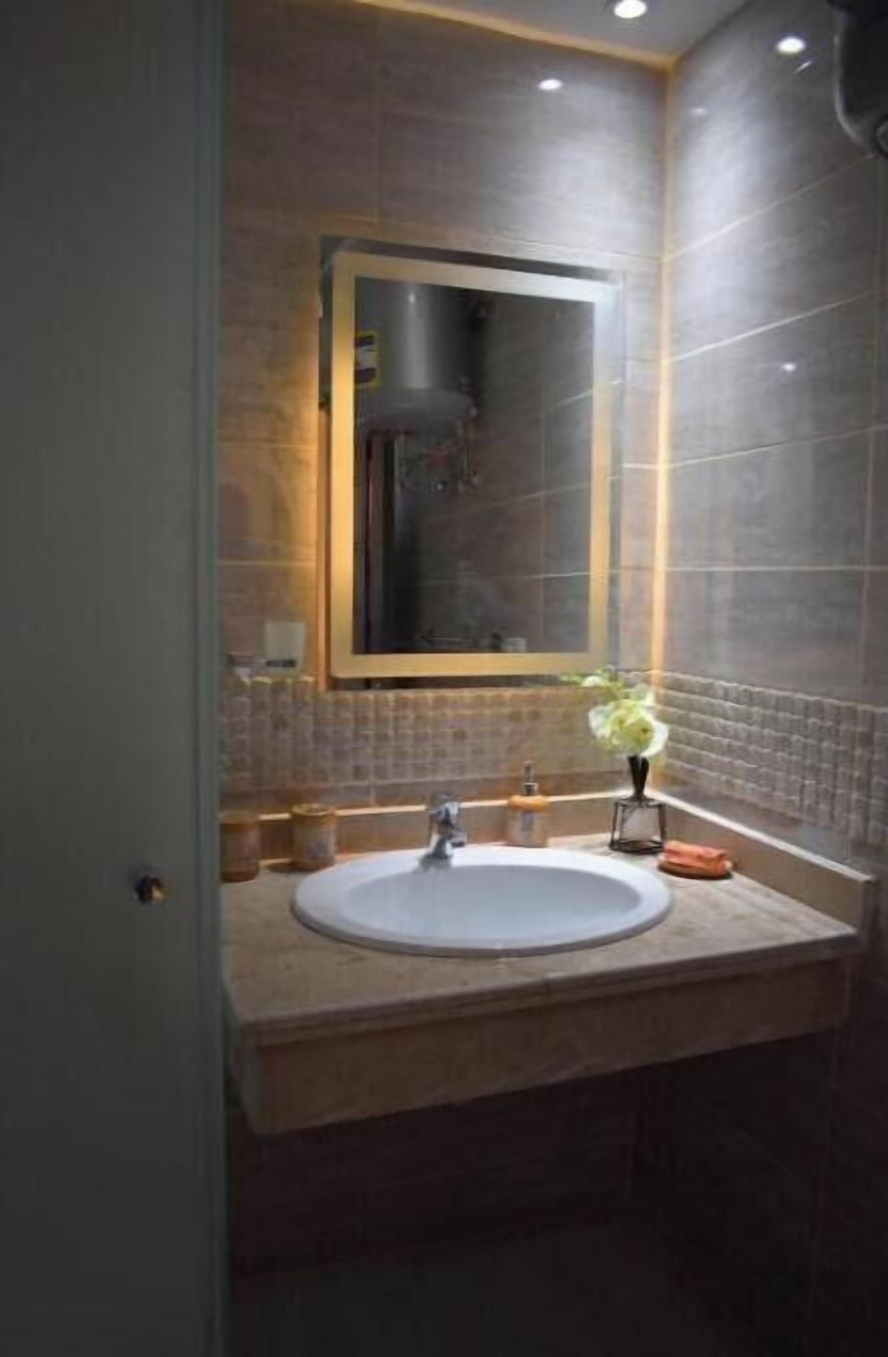 Une salle de bain avec un grand miroir, un lavabo et un vase rempli de fleurs.