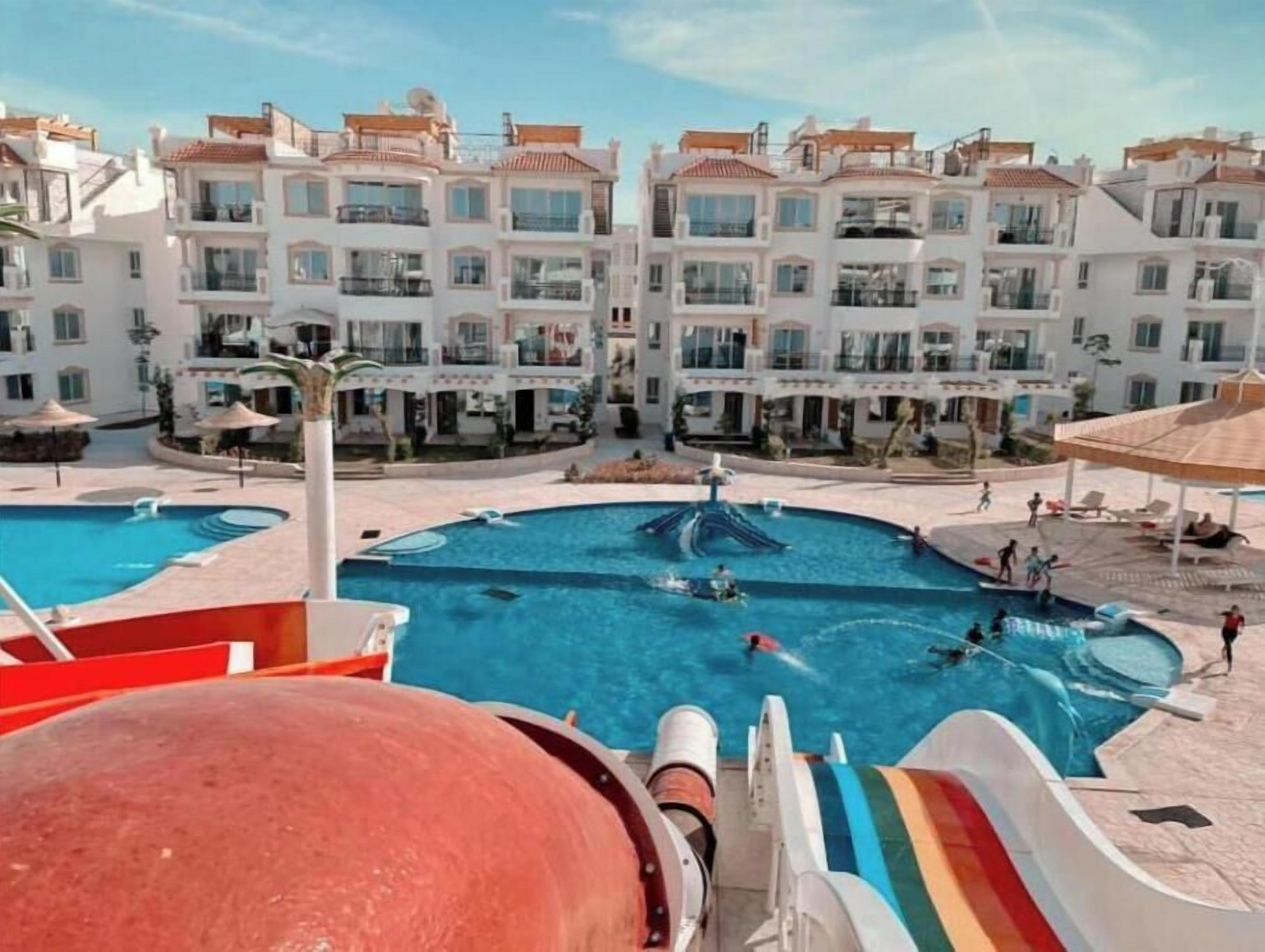 Un resort con varias piscinas, un tobogán y vistas de los edificios circundantes.