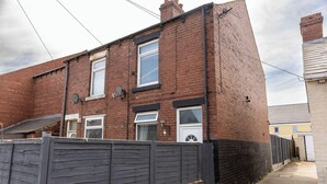 A two-story brick house with a dark wooden fence in front. - Victoria Road Retreat - Charming 2 Bedroom House (Barnsley)