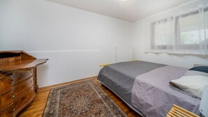 A bedroom with a bed, a wooden dresser, a radiator, and a window with sheer curtains. - GuestHost - Cozy Apartment with Terrace - Tarvisio (Tarvisio)