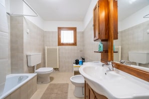 Un baño con bañera, dos inodoros, un lavabo, un espejo y una ventana.