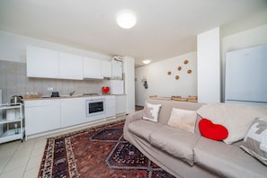 A modern kitchen with white cabinets, a red kettle, and a patterned rug.