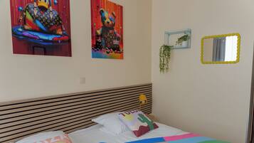 A bedroom with a bed, pillows, a headboard, a wall-mounted mirror, and two wall art pieces.