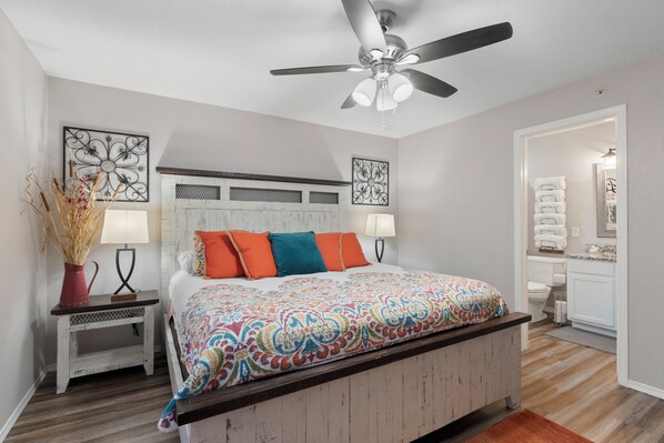 A bedroom with a bed, bedside tables, a ceiling fan, and a bathroom visible through an open door.