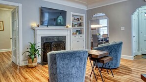 Una sala de estar con chimenea, un televisor montado sobre ella y un comedor con una mesa y sillas.