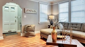 Un salón con un sofá color beige, una mesa de centro con un florero y una puerta con interruptor de luz.