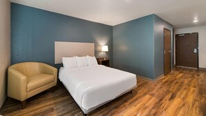 Ein Hotelzimmer mit Bett, Stuhl, Nachttisch und Tür.