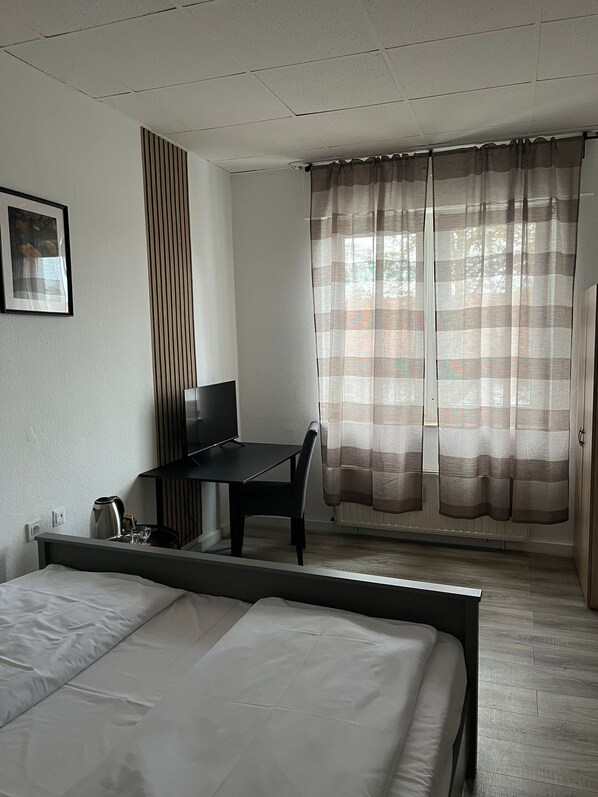 A bedroom with a bed, a desk, a chair, a television, and a window with curtains. - Art Rock Airport Hotel (Cologne)