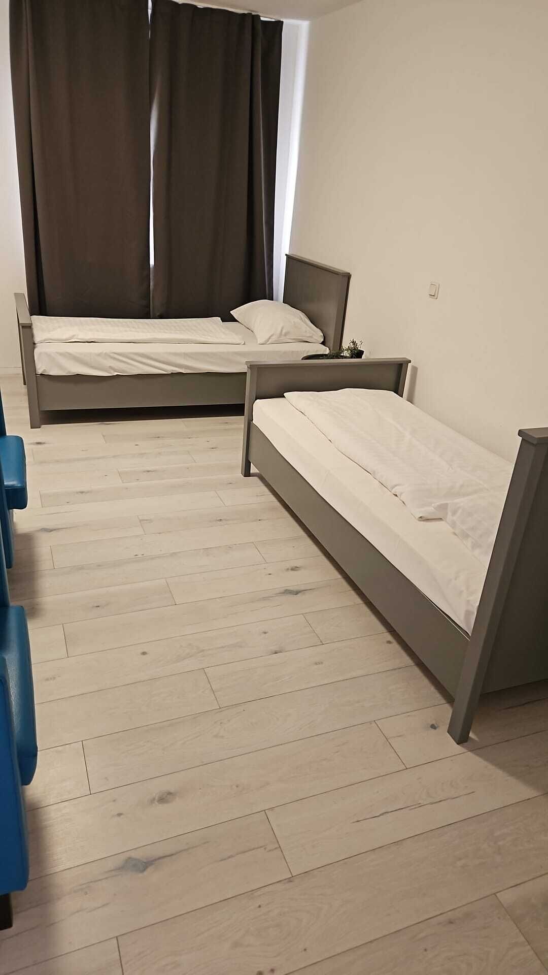 A room with two single beds, a blue chair, and a window with curtains.