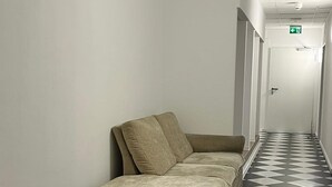 Un couloir avec un sol à carreaux, un canapé beige et une petite table sur laquelle se trouve un pot.