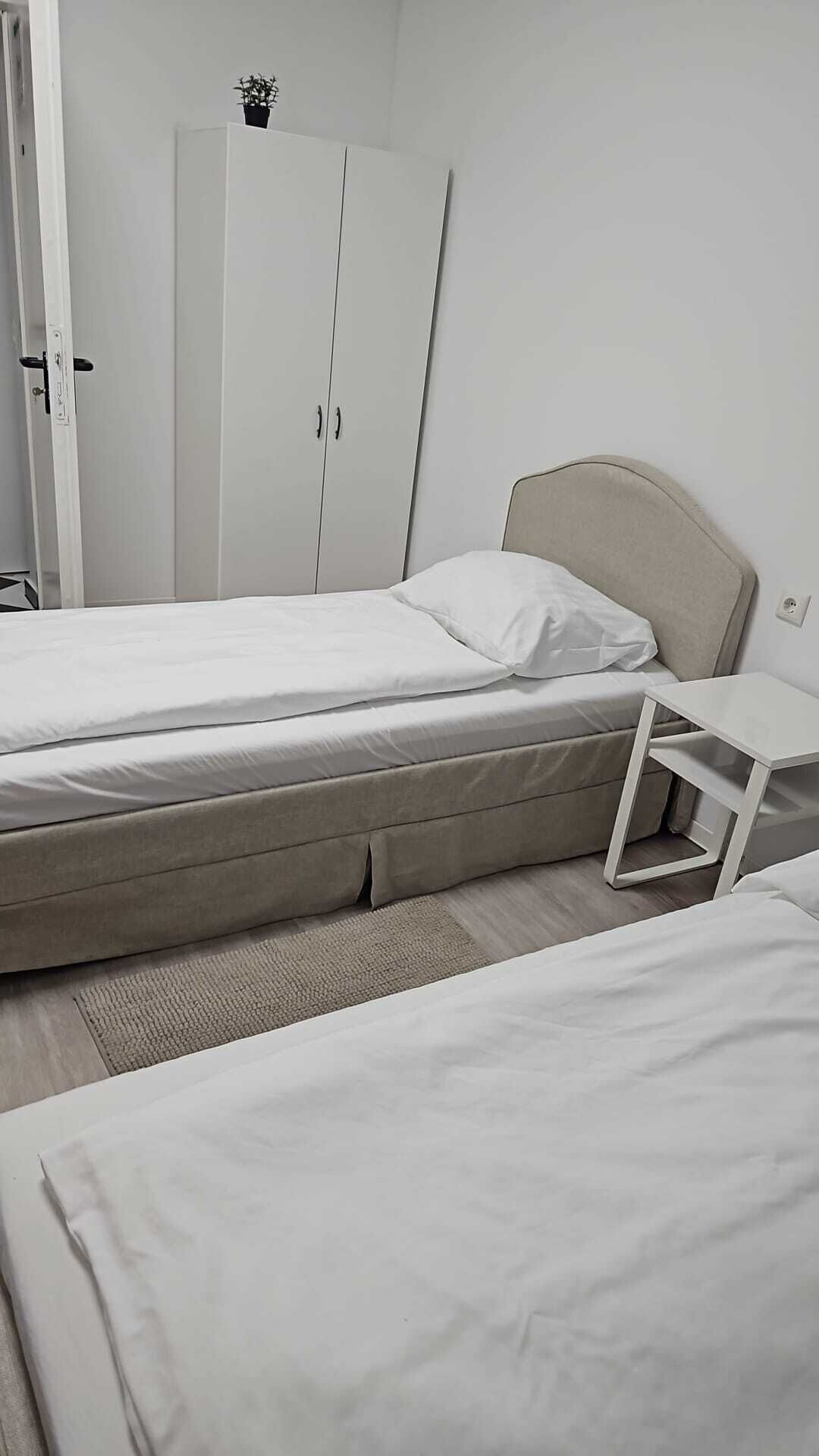 Quarto de hotel com duas camas, uma mesa de cabeceira, um guarda-roupa e um vaso de planta.