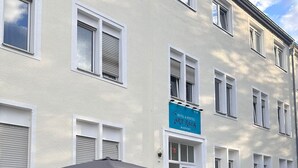 Façade d’un hôtel avec un patio comprenant une table et des chaises, un grand parasol et une enseigne indiquant qu’il s’agit de l’hôtel et de l’auberge de jeunesse Art Rock Airport.