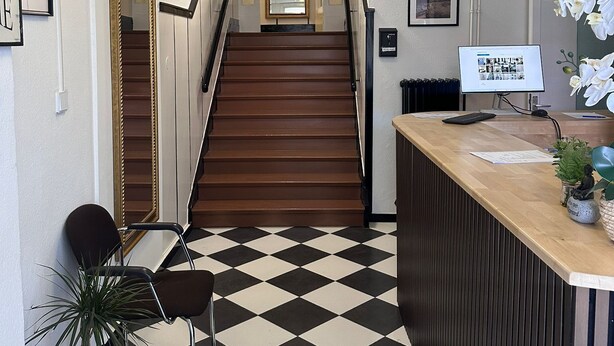 Un espace d’accueil avec un sol à carreaux, un escalier, un comptoir d’accueil et une plante en pot.