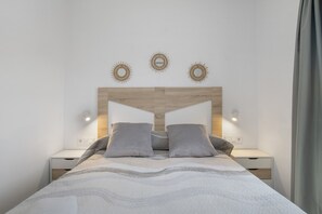 Een moderne slaapkamer met een houten hoofdbord, twee nachtkastjes, een bed met grijze beddengoed en wandlampen.