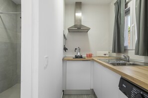 Une cuisine compacte équipée d’un lave-vaisselle encastré, d’une machine à café et d’un évier en acier inoxydable.