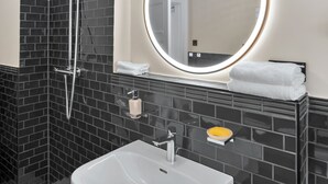 Ein Badezimmer mit einem weißen Waschbecken, einem Spiegel mit Beleuchtung und einer Dusche.