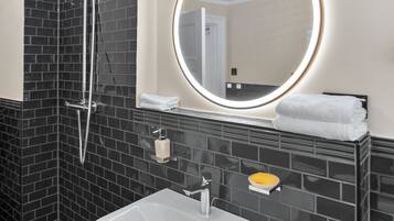 Ein Badezimmer mit einem weißen Waschbecken, einem Spiegel mit Beleuchtung und einer Dusche.