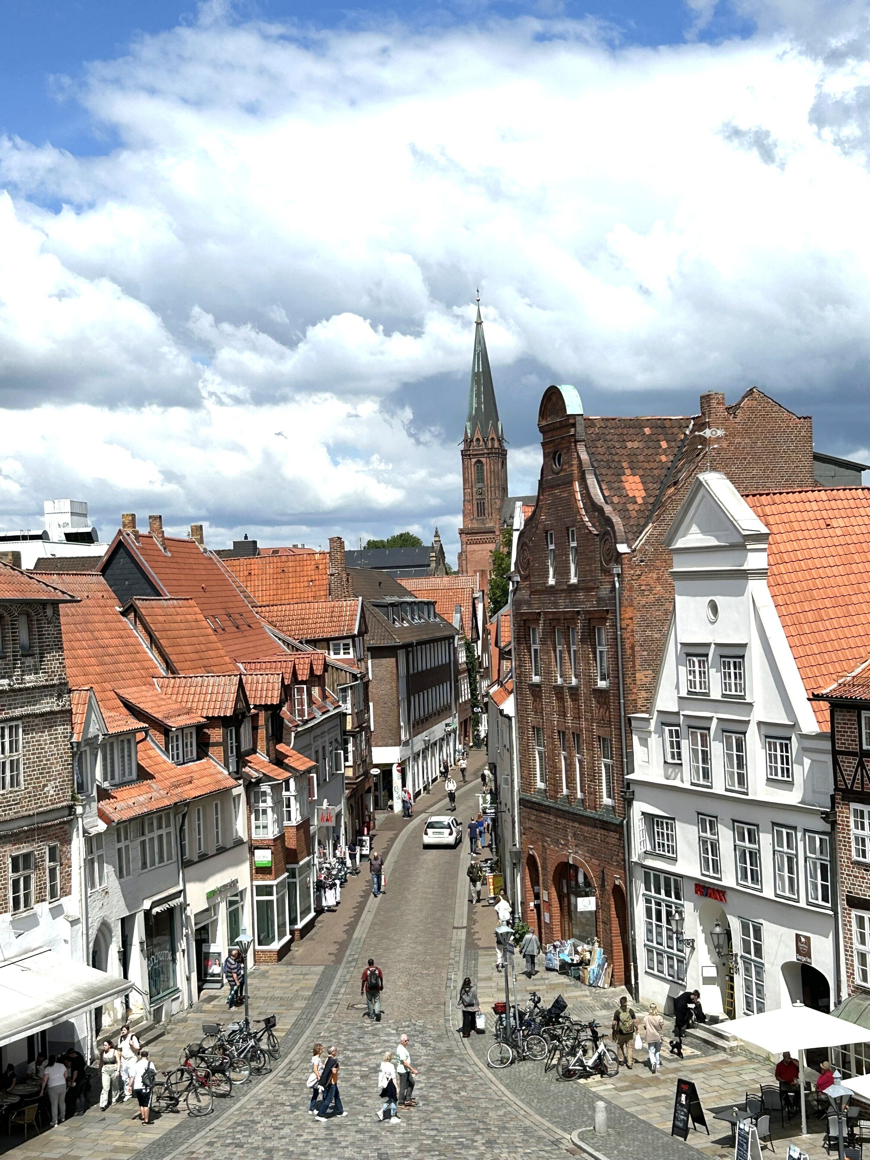 A cobblestone street lined with historic buildings, including a prominent church tower and a traditional half-timbered house.