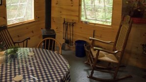 Interior acogedor de una cabaña con una mesa redonda, paredes de madera y ventanas grandes con vistas al bosque.