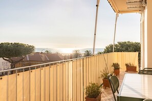A balcony with a view of the sea, potted plants, and a table with chairs.