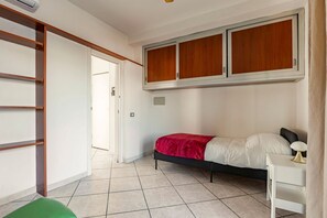 A bedroom with a bed, a desk, a wardrobe, and a door leading to another room.