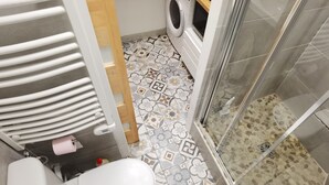 A bathroom with a toilet, washing machine, and shower area.