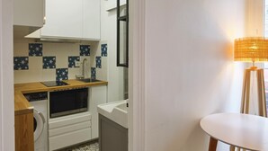 A compact kitchen with white cabinets, a wooden countertop, a built-in oven, and a washing machine.