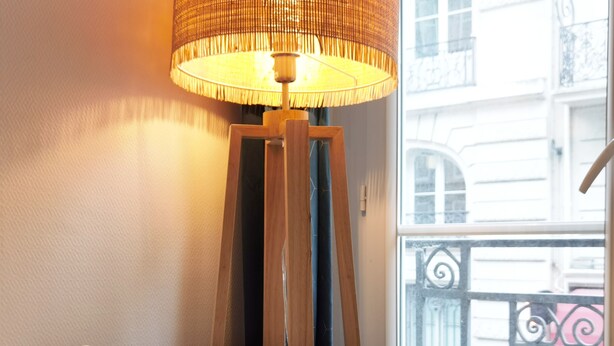 A room with a white table, a small white bear figurine, a tall floor lamp, and a view of a balcony with a wrought iron railing.
