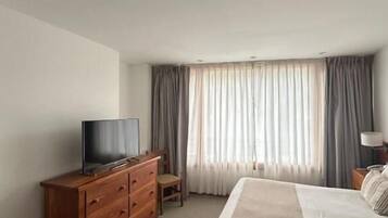 A hotel room with a bed, a wooden dresser, a television, and a window with curtains.
