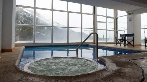 A large indoor swimming pool with a hot tub, large windows, and a view of snow-capped mountains. - Hosteria del Cerro (San Carlos de Bariloche)