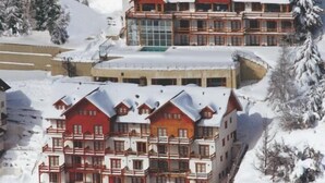A large, multi-story hotel with a red and white exterior, surrounded by snow-covered trees and hills. - Hosteria del Cerro (San Carlos de Bariloche)