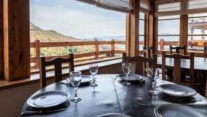 A dining table set for four with a scenic view of hills and mountains through large windows. - Hosteria del Cerro (San Carlos de Bariloche)