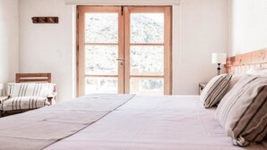 A bedroom with a large bed, a wooden headboard, a chair with striped cushions, and a window with a mountain view. - Hosteria del Cerro (San Carlos de Bariloche)