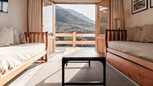 A room with two beds, a table, and a balcony with a mountain view. - Hosteria del Cerro (San Carlos de Bariloche)