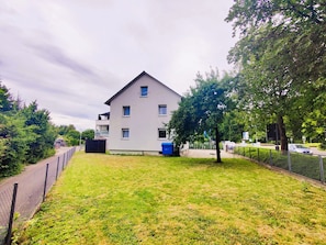 A two-story residential building with a flat roof, a fenced yard, and a blue dumpster.
