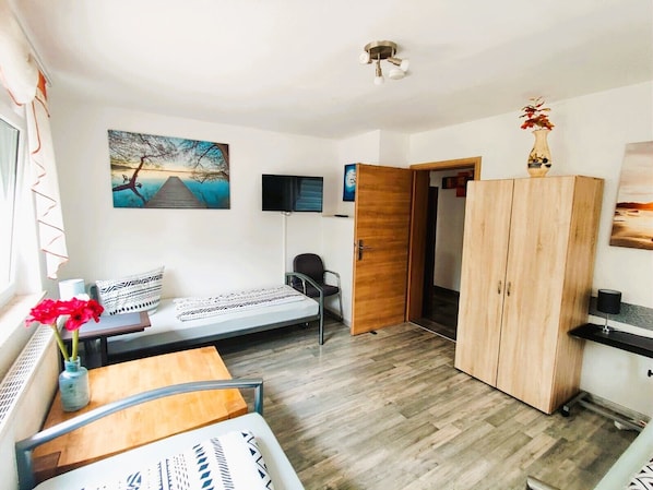 A room with a bed, a desk, a chair, a wardrobe, a TV, and a painting.