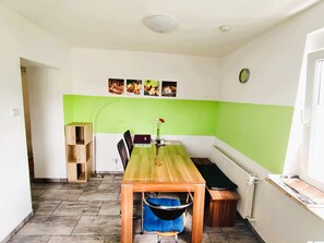 A dining area with a wooden table, chairs, a bench, a radiator, and a clock on the wall.