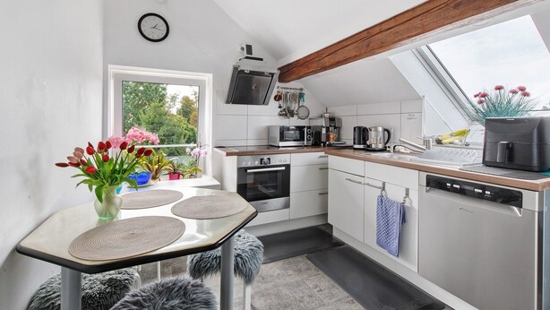Een moderne keuken met dakraam, een eethoek met tafel en stoelen, en uitzicht op groen.