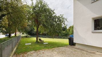 A residential area with a paved driveway, a bench, a tree, and a building with a window.