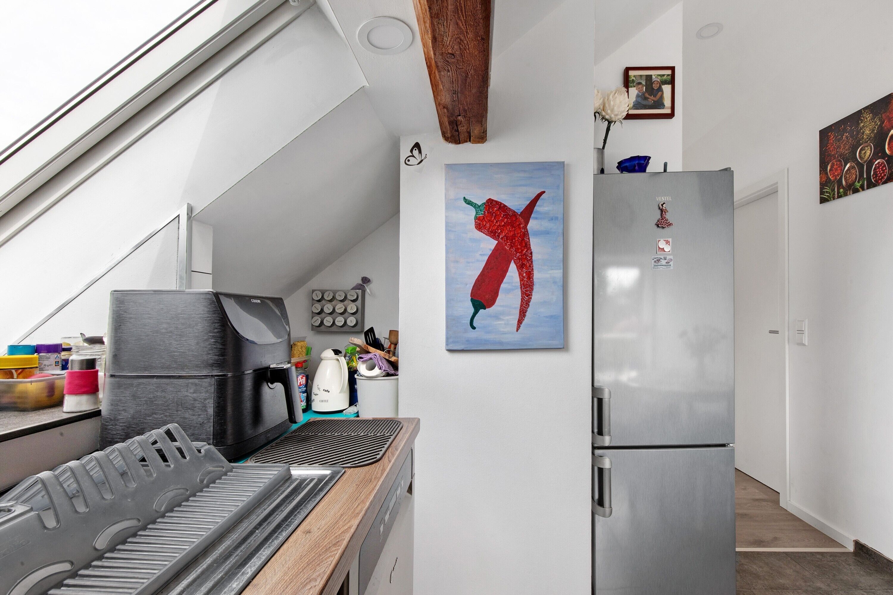 Une cuisine moderne équipée d’un four encastré, d’un réfrigérateur et ornée d’un tableau représentant un piment sur le mur.