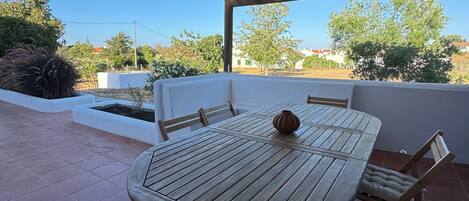 A wooden table with chairs and a vase, set on a tiled patio with a bamboo ceiling.