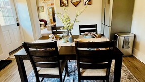 A dining area with a wooden ceiling, a chandelier, a dining table set with chairs, and a refrigerator.