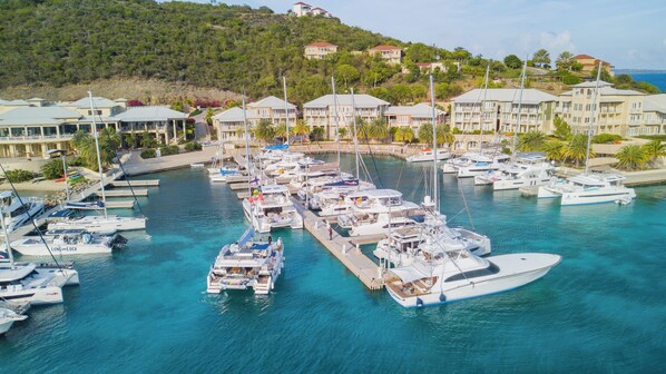 Un puerto deportivo con varios yates amarrados, rodeado de edificios residenciales y un paisaje montañoso.