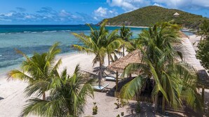 Una playa con agua turquesa cristalina, palmeras y una cabaña con techo de paja.