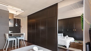 Een moderne hotelkamer met een groot bed, een bureau met twee stoelen, een donkere scheidingswand en een afgescheiden slaapgedeelte met hoofdbord.