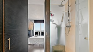 Een moderne hotelkamer met een groot bed, een douche met glazen deur en uitzicht op de stad.