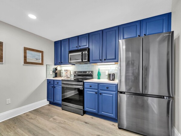 A modern kitchen with blue cabinets, stainless steel appliances, and a tiled backsplash.