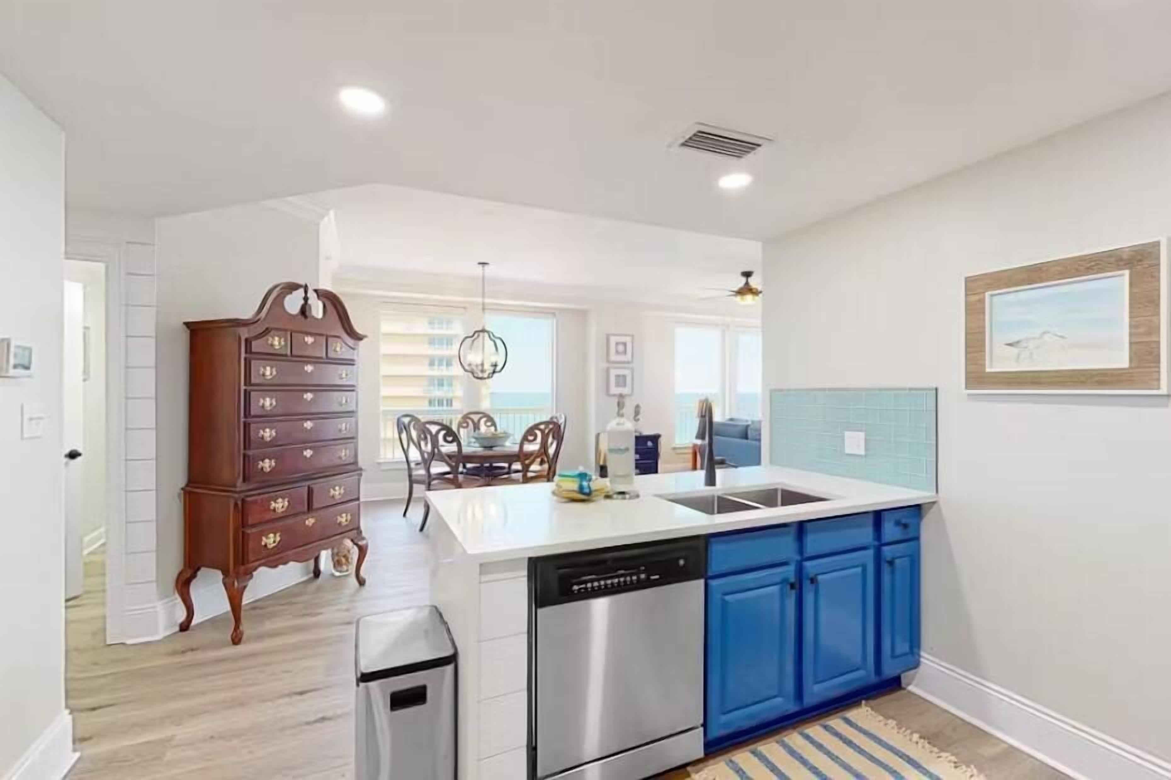 A modern kitchen with a dishwasher, blue cabinets, and a wooden dresser.