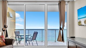 A room with a large sliding glass door leading to a balcony with a view of the sea. There is a sofa, a table, and chairs on the balcony. - Majestic Beach Towers 1-2003 (Panama City Beach)